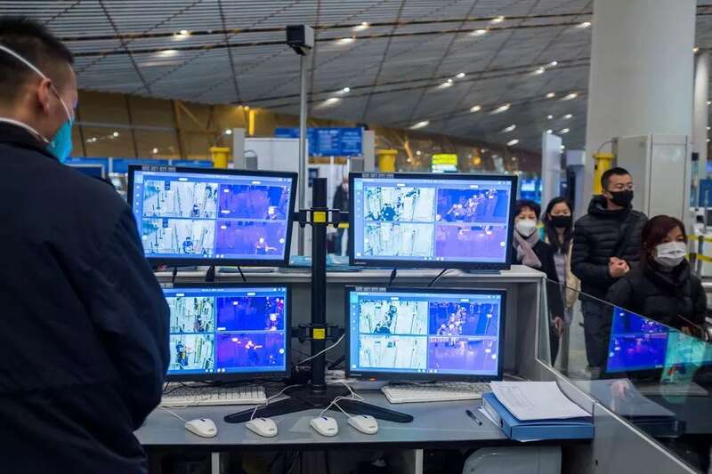 在北京首都国际机场，一名工作人员在人们戴着口罩抵达机场时监控热扫描仪 ...